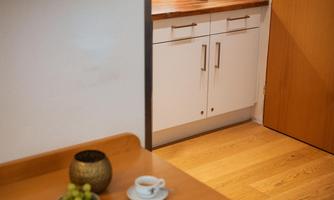 A cozy corner with a wooden table and a cup of coffee. In the background, there is a modern kitchen unit with a coffee machine.