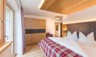 A cozy bedroom with a large bed and a wooden ceiling. There is a wardrobe and a window that provides plenty of light.