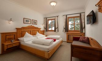 A cozy bedroom with wood furniture and a large double bed. The windows offer a view of nature and provide plenty of daylight.