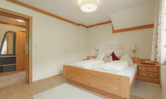 A cozy bedroom with a wooden bed and bright walls. The room is simply furnished and has a friendly atmosphere.