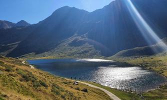 A scenic mountain lake surrounded by tall mountains. The sun reflects on the water's surface, creating a tranquil atmosphere.