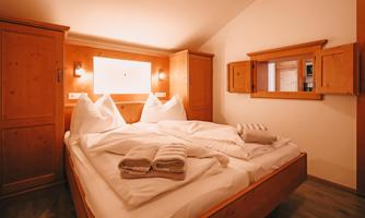 A cozy bedroom with a double bed and wooden wardrobes. Fresh towels are neatly stacked on the bedspread.