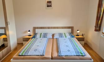 A cozy bedroom with a double bed and colorful blankets. Nightstands with lamps and a mirror in the corner can be seen.
