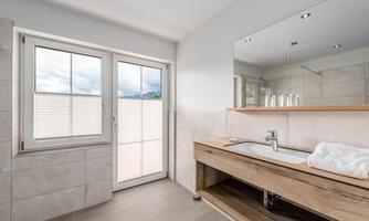 A modern bathroom with a wooden sink and large windows. The bright, neutral color palette creates an inviting atmosphere.