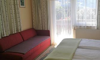 A cozy bedroom with a double bed and a red sofa. Large windows let in plenty of daylight.