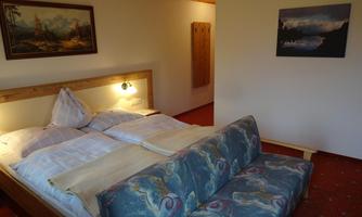 A cozy room with a double bed and a comfortable sofa. Pictures of landscapes hang on the wall.
