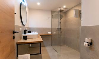 A modern bathroom with a glass shower and a sink on a wooden shelf. The walls are in neutral colors and the light is bright and inviting.