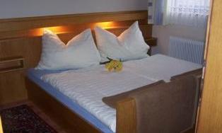 A cozy bedroom with a large bed and white pillows. A small floral decoration lies on the bed.