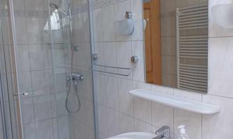 A modern bathroom with a shower cabin and a sink. The walls are tiled and the decor is bright and functional.