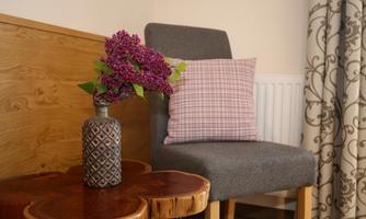 A cozy chair with a checkered cushion stands next to a round wooden table. A vase with purple flowers adds a nice accent to the room.