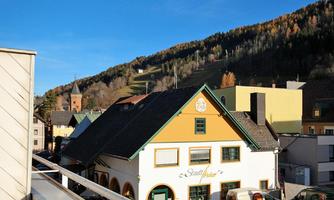 A picturesque town view with colorful buildings and autumn-colored trees in the background. The clear sky and mountains give the scene a tranquil atmosphere.