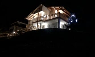 A beautiful house at night, illuminated by warm light. In the foreground, a lit tree is visible.