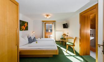 A bright room with two beds, a table, and a television. The room has access to a balcony and a modern decor.