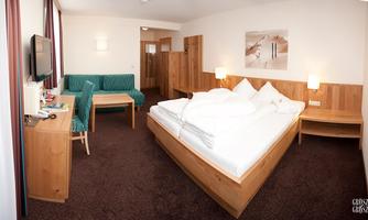 A cozy hotel room with a large bed and a seating area. The walls are light, and the furniture is made of wood.