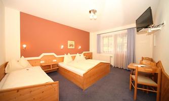 A comfortable bedroom with two separate beds and a table. The walls are painted in soft colors, and a television is mounted on the wall.