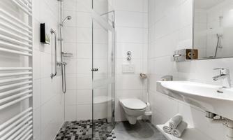 A modern bathroom with a glass door shower and a white sink. The walls are tiled and the floor has a stylish pattern.