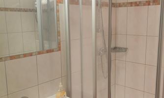 A modern shower with a glass partition. The room is tiled and features a sink.