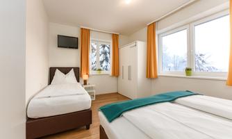 A bright room with two beds and orange curtains. Through the window, you can see a snowy landscape.