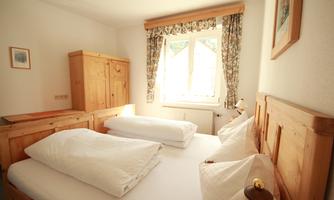A cozy bedroom with two beds and wooden furniture. The window lets in plenty of daylight and the room is furnished in a friendly manner.