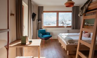 A modern bedroom with a double bed and a loft bed. The windows offer a view of the mountains.