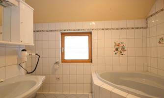 A bathroom with a bathtub and a sink. A window provides natural light and a bright, friendly atmosphere.