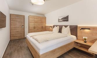 A modern bedroom with wood decor and a double bed. The walls are light, and the lighting creates a pleasant atmosphere.