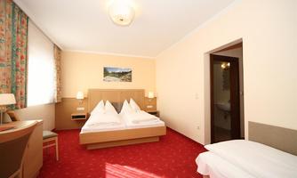 A cozy hotel room with a double bed and a single bed. The walls are light and the room has large windows with a view of the landscape.