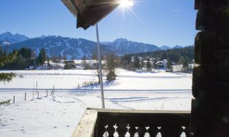 A snowy landscape with mountains in the background and a clear blue sky. The sun shines brightly over the winter scene.