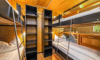 A cozy sleeping area with bunk beds and wood paneling. The room contains shelves and large windows that let in light.