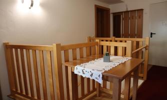 A cozy room with a wooden table and a tablecloth. The area is separated by wooden railings and has a warm atmosphere.