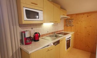 A modern kitchen with wooden cabinets and bright walls. It is equipped with a stove, a microwave, and various kitchen utensils.