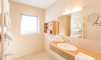 A modern bathroom with a bright design and large windows. There is a wooden vanity top and neatly arranged towels.