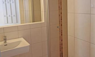 A modern bathroom with white tiles and a sink. On the right side, there is a shower with a glass door.