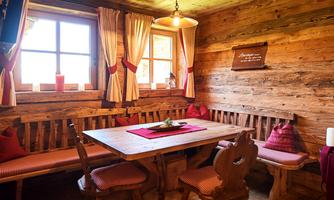 A cozy dining area with wooden paneling and simple furniture. There is a window with curtains and a decorated tabletop.