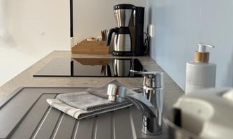 A modern kitchen with a faucet, a stove, and a coffee machine. The walls are light blue and the countertop is made of gray material.