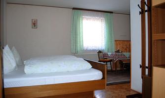 A simple room with a double bed, a table, and chairs. It has a window with curtains that lets in daylight.