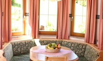 An inviting dining room with a rounded corner and a table in the center. A fruit bowl is placed on the table, while the windows are decorated with pink curtains.