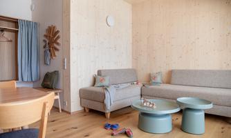 A modern living room with wooden paneling and light furniture. There is a cozy seating area and a dining table.