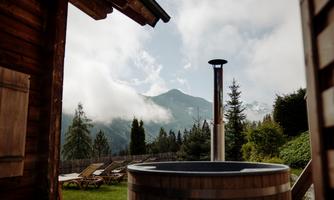 An outdoor bathtub with a view of the mountains and clouds. Surrounded by trees and a cozy atmosphere.