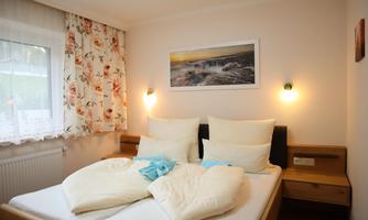 A cozy bedroom with a double bed and bright pillows. A picture hangs on the wall and there is soft light from the wall lamps.