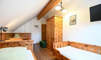 A bright room with wooden furniture and slanted walls. There are two beds, a wardrobe, and a window that provides daylight.