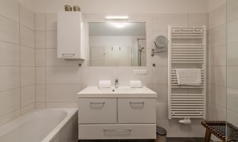 A modern bathroom with a bathtub and a sink. The walls are brightly tiled, and there is a towel rack as well as a mirror light.