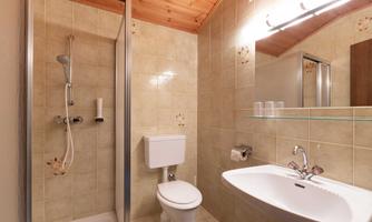 A modern bathroom with a shower, toilet, and sink.  
Walls with bright tiles and a wooden ceiling.