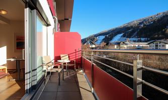 A balcony with two chairs and a table. In the background, there are snow-capped mountains and a clear blue sky.