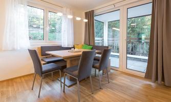 A cozy dining area with a wooden table and modern chairs. Large windows provide a view of the outdoor area.