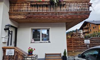 A pretty house with a balcony decorated with flowers. In the foreground, there is a bench next to the front door.