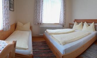 A bright room with two single beds and a double bed. The walls are adorned with curtains and there is a small table in the corner.