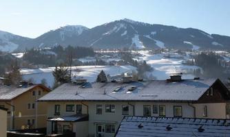 A picturesque winter landscape with snow-covered mountains in the background. In the foreground, various houses with snow-covered roofs can be seen.