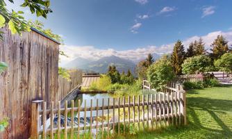 A picturesque landscape with a pond, surrounded by lush greenery and trees. In the background, majestic mountains rise under a clear sky.