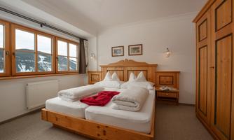A cozy bedroom with a double bed and wooden furniture. Large windows offer a view of the surrounding landscape.